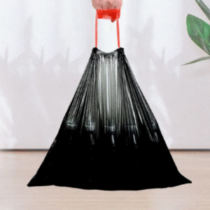 The black biodegradable bag is displayed hanging, with a red drawstring at the bag mouth, giving the bag a strong drape. The background is decorated with green plants, highlighting the product material and practical design.