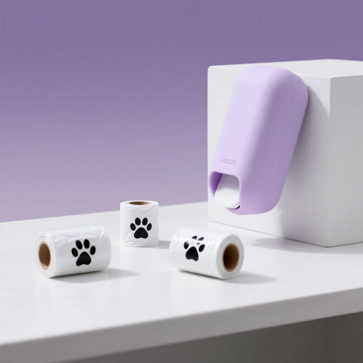 Four rolls of white pet waste bags with black paw prints are placed on a light purple background to highlight the product packaging design.