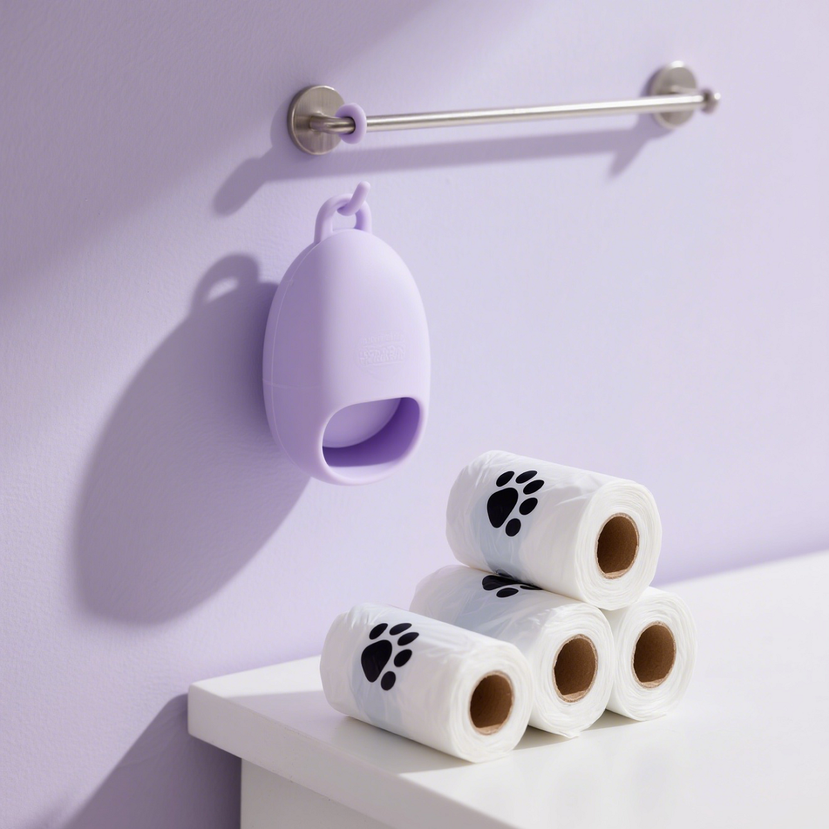 A silver rod hangs on the light purple wall, with three rolls of pink pet waste bags with black paw prints, showing product storage and display.