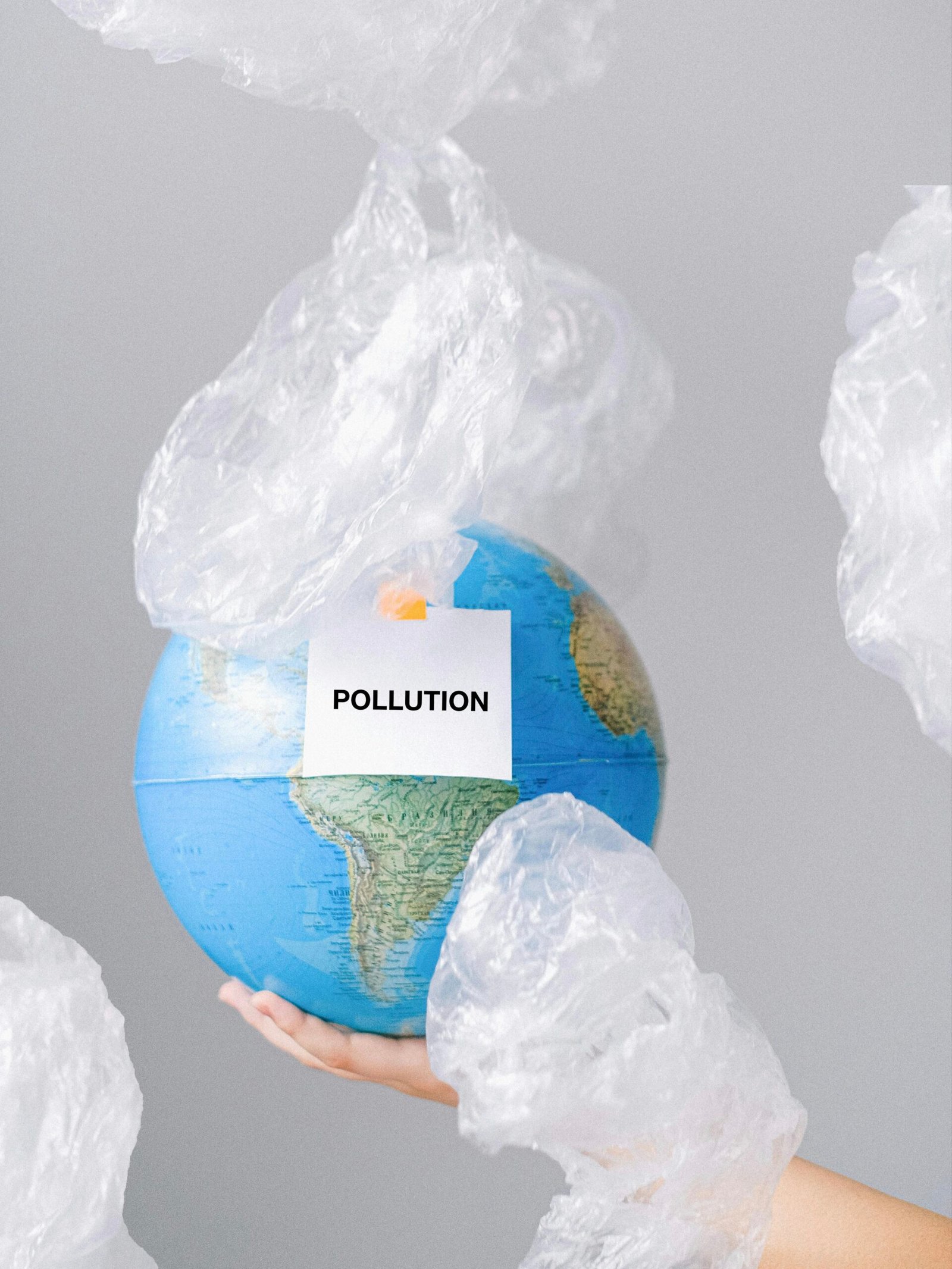 Plastic pollution environmental concept: hand holding Earth globe covered in plastic waste, labeled POLLUTION, visual for white pollution and climate crisis awareness.