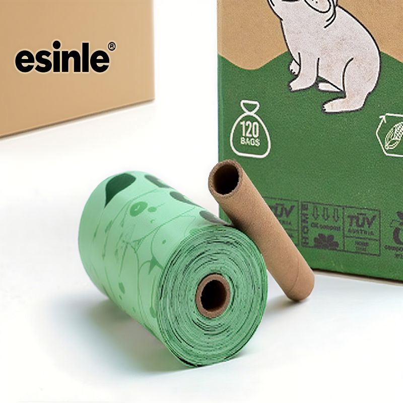 A green roll of “esinle” branded film with a cardboard tube, beside a green box featuring an eco-icon, is representing eco-friendly, biodegradable packaging or pet waste solutions for sustainable use.