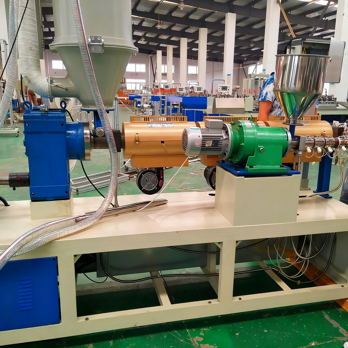 A large factory workshop with green flooring, various blue and metallic machinery, and spacious layout, indicating an organized environment for plastic film or packaging material production.