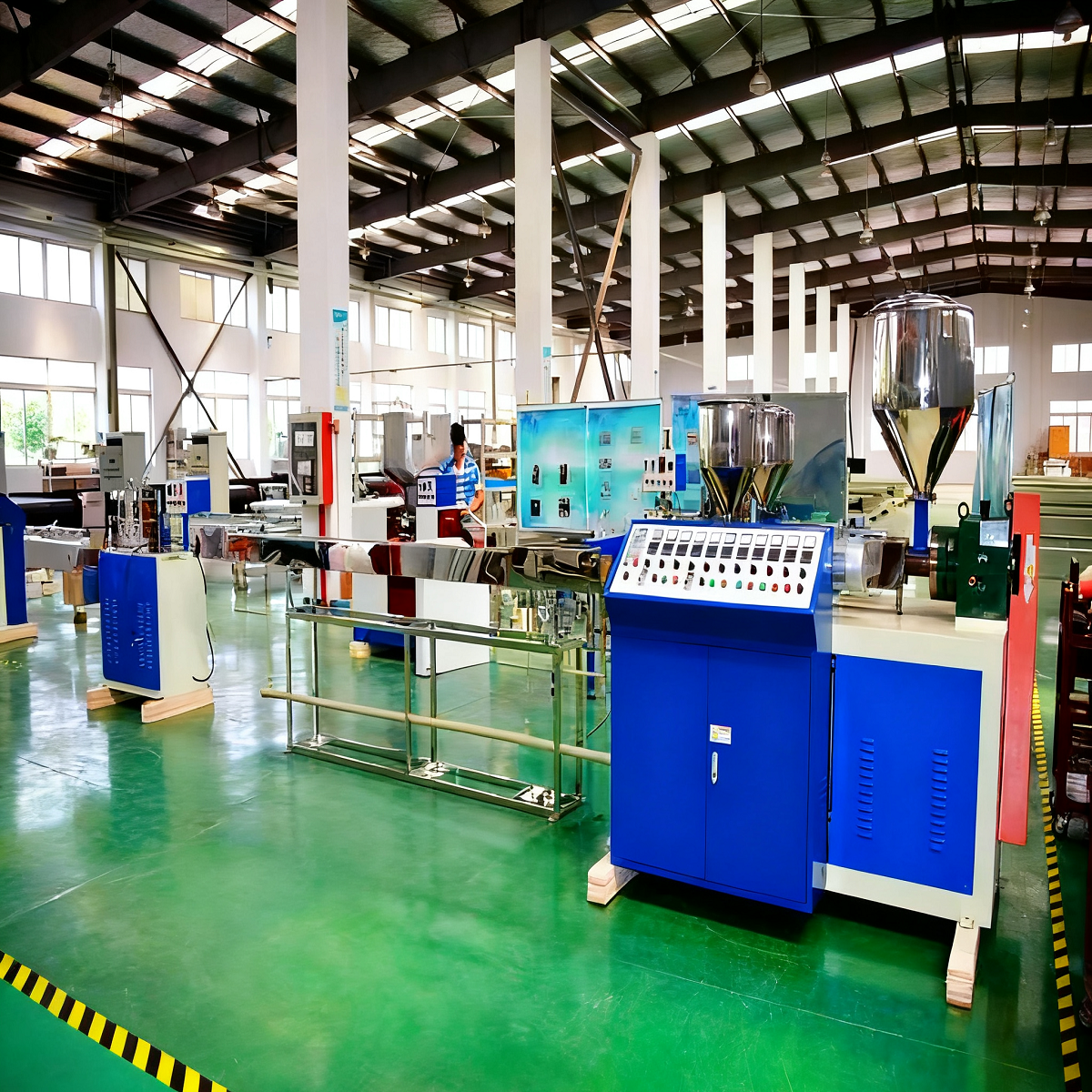 A large factory workshop with green flooring, various blue and metallic machinery, and spacious layout, indicating an organized environment for plastic film or packaging material production.