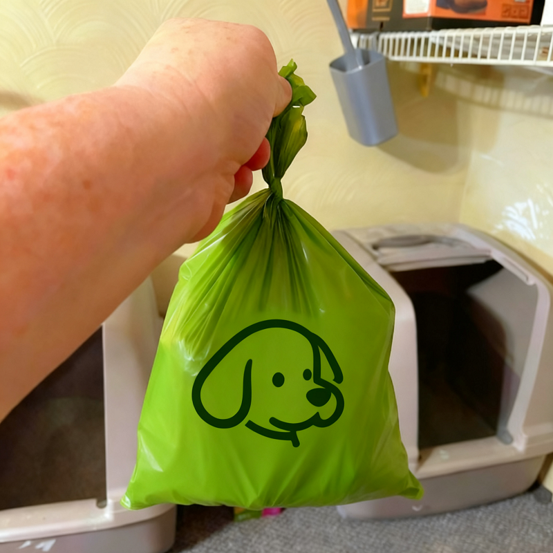 A hand tying a green bag with a dog graphic, is an biodegradable pet waste bag, demonstrating sustainable waste management for pet owners.