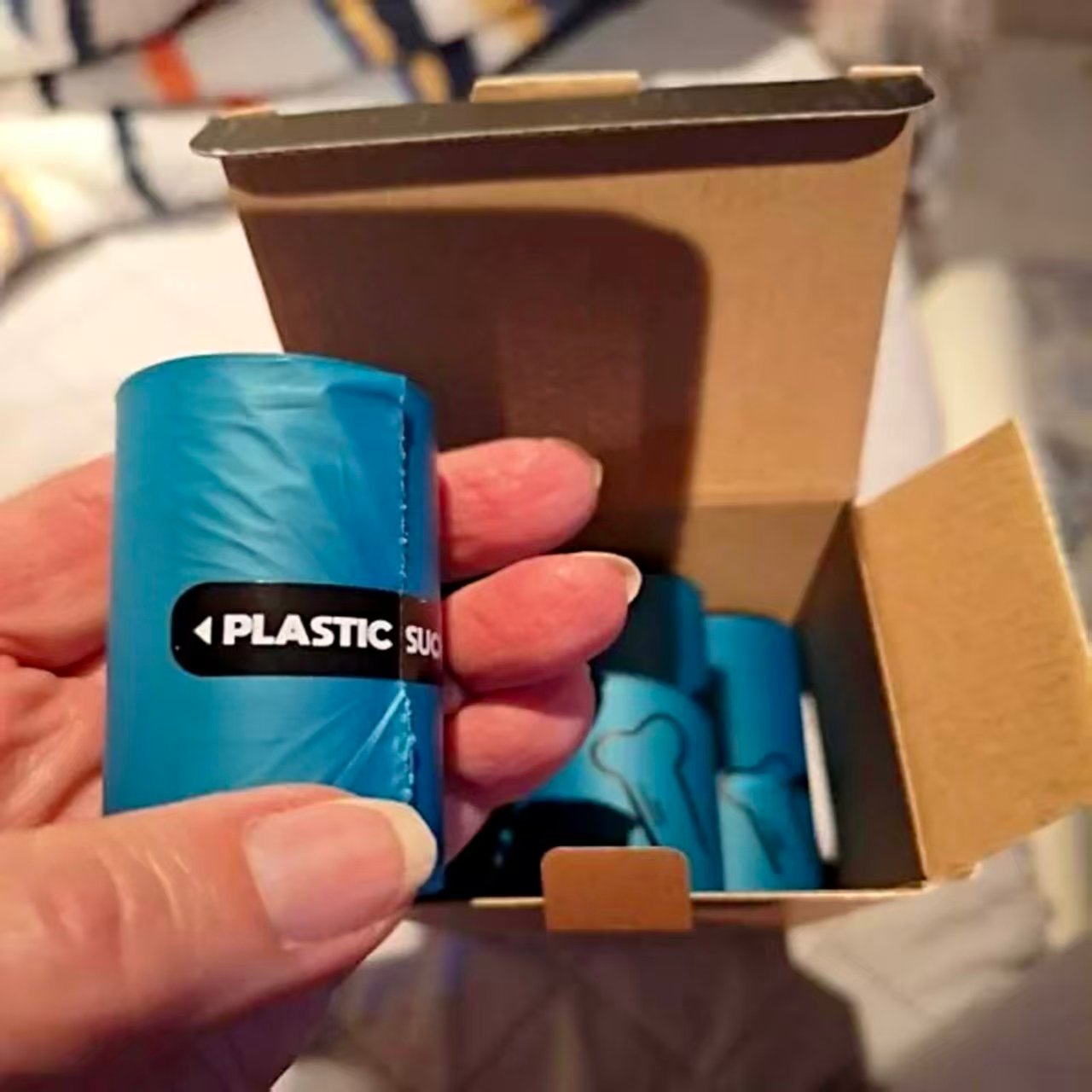 Customer holding blue biodegradable dog poop bag roll from cardboard box with PLASTIC SUCKS label - ESINLE eco-friendly pet waste bags