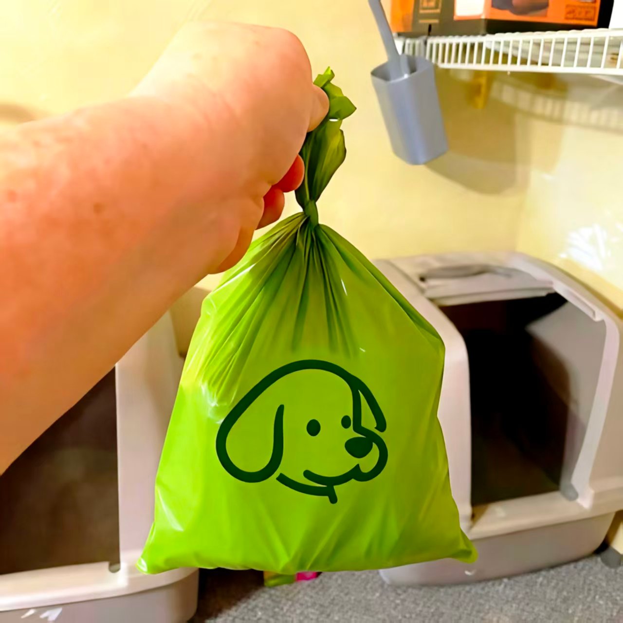 Hand holding tied green biodegradable dog waste bag with cartoon dog logo near pet litter box - ESINLE customer review