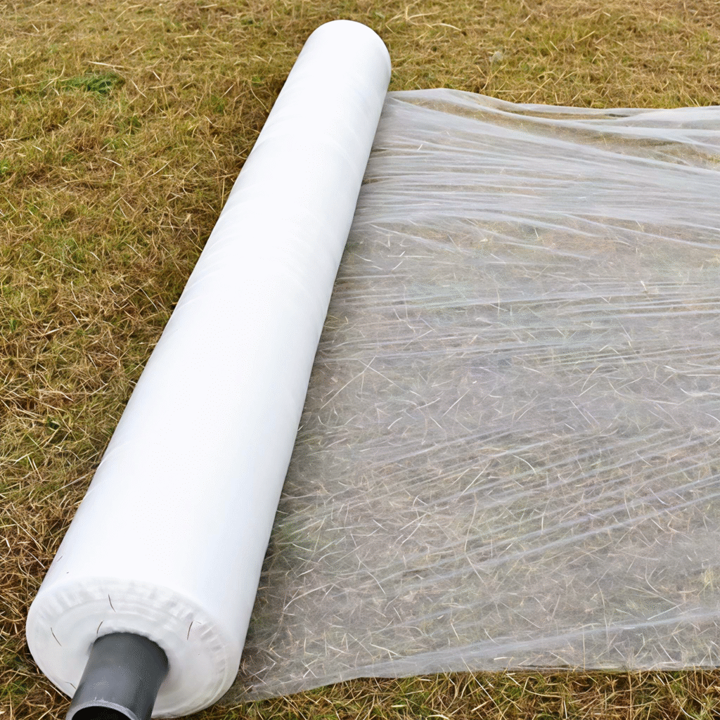Large roll of translucent biodegradable film unrolled on dry grass field, showing texture and transparency, suitable for agricultural mulch or temporary ground cover