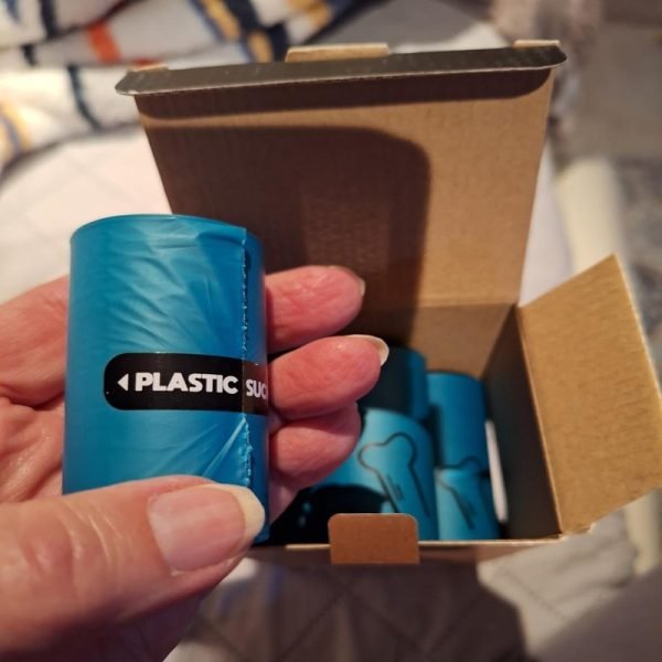 A hand holding a blue “3-Roll Pack” of plastic film rolls inside an open cardboard box, use for eco-friendly storage or packaging, showcasing compact and sustainable wrapping solutions.